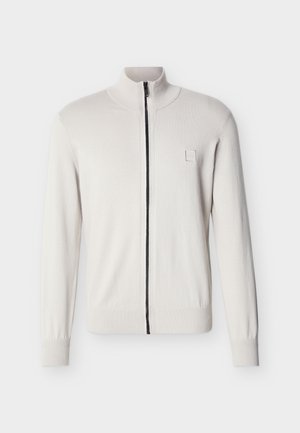 Weißer Pullover mit durchgehendem Reißverschluss, gerippten Bündchen und Saum, Stehkragen und einem kleinen, quadratischen Logo-Patch auf der linken Brust.