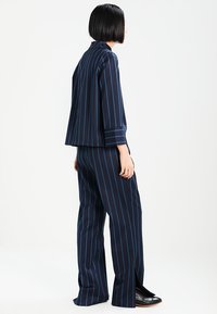 Completo a righe blu navy con pantaloni a gamba larga e giacca corta a maniche corte, dalla vestibilità rilassata. Presenta strisce verticali blu a contrasto. Tessuto liscio.