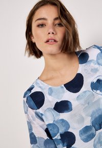 Blue and white patterned blouse featuring watercolor-style circular designs, a round neckline, and lightweight fabric with a textured finish.