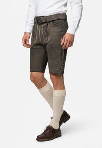 Bruna läderlederhosen med broderade blommönster, kontrasterande gul sömnad och sidoknytning. Sammansatt med beige knähöga strumpor och bruna skor.