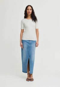 Bela rebrasta majica s kratkimi rokavi v kombinaciji z dolgo modro jeans krilo s sprednjim razporkom, dopolnjena s črnimi sandali na peto.