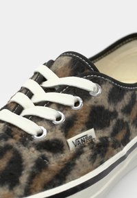 Brown and black leopard-print Vans shoes with white laces, featuring metallic eyelets and a cream interior. Textured surface, rubber sole.