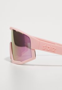 Rosa Sport-Sonnenbrille mit matter Oberfläche, sechseckigen Gläsern in lila Verlauf und geprägtem Logo am Bügel.