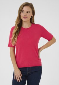 Short-sleeve, crew neck t-shirt in bright pink fabric, featuring a textured finish and relaxed fit, paired with dark denim jeans.