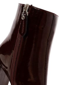 Bottine en cuir verni bourgogne avec une finition brillante, fermeture éclair sur le côté avec quincaillerie en argent, et couture rouge contrastante le long de la couture.