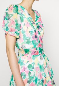 Blumen-Wickelkleid mit V-Ausschnitt, Puffärmeln und tailliertem Schnitt. Der Stoff ist leicht und zeichnet sich durch lebendige grüne, pinke und gelbe Farbtöne aus.