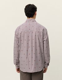 Camisa abotonada con rayas verticales rojas y blancas, que presenta pequeños patrones florales en marrón, mangas largas y un cuello estándar.