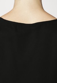 Vêtement noir avec un large décolleté et une texture lisse, montrant le dos du vêtement, avec un détail de couture minimal.