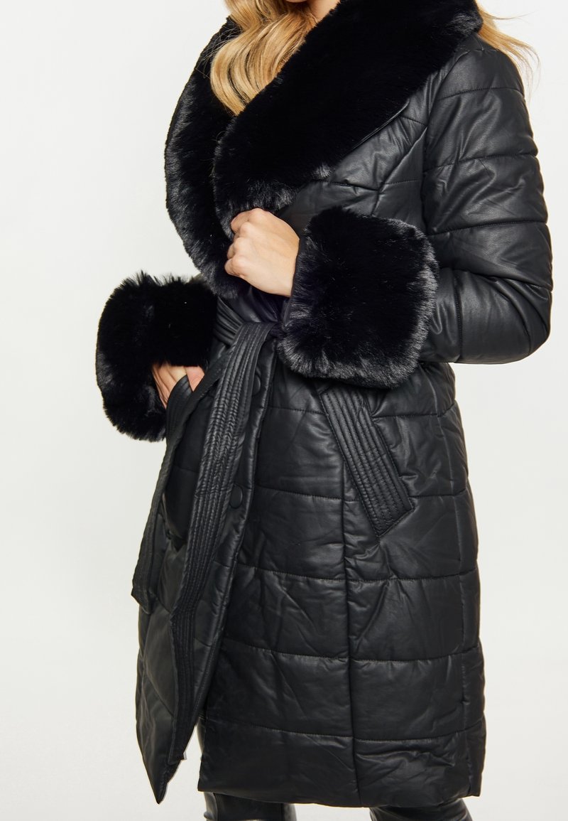 Czarny pikowany płaszcz z sztucznym futerkiem na kołnierzu i mankietach. Posiada pasek w talii i boczne kieszenie, tkanina jest błyszcząca i teksturowana.
