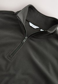 Tumši pelēks kvadrāta rāvējslēdzēja džemperis izgatavots no mīksta auduma. Tam ir gluda virsma, stāvošs apkaklis un metāla rāvējslēdzējs ar auduma vilkšanas cilpu.