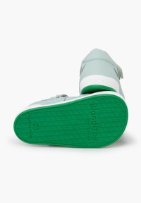 Suela de goma verde con agarre texturizado, parte superior sintética de color gris claro, con cierre de tiras de velcro y detalles en blanco en el talón y la suela.