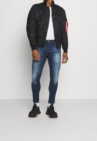 Black bomber jacket with a zip and pockets, white T-shirt, distressed blue skinny jeans, and black sneakers with pink accents.
