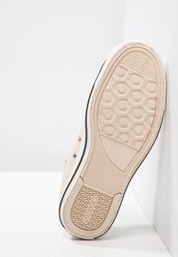 Sneaker in tela beige con suola in gomma texturizzata, bordature nere e un motivo a tasto esagonale sul fondo per una maggiore aderenza.