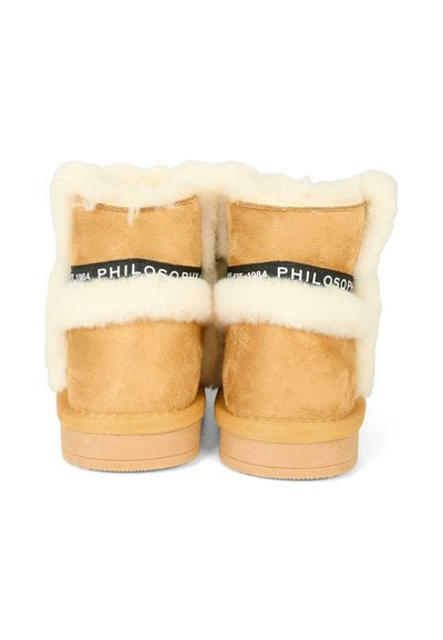 Stivali alla caviglia in suede beige con fodera in morbido pellicciotto bianco. Presentano una cintura nera con etichetta "PHILOSOPHY EST. 1984" e una suola in legno piatta.