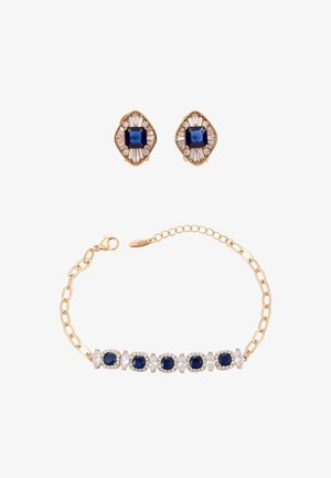 Ensemble de bijoux ton or avec pierres précieuses bleu profond. Comprend un bracelet avec des pierres bleues et transparentes alternées, et des boucles d'oreilles assorties avec un design décoratif.