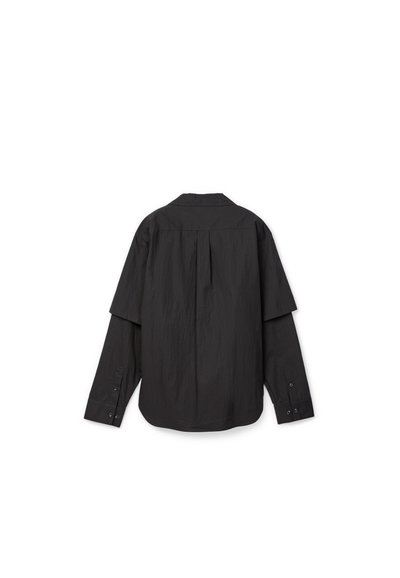 Camisa negra de manga larga mostrada desde atrás con un detalle de solapa superpuesta en los hombros y puños con botones.