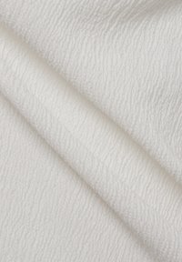 Tissu blanc texturé avec un motif ondulé, finition douce et légère brillance, plié pour montrer les couches et la profondeur.