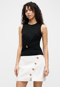 Μαύρο αμάνικο τοπ με σπειροειδές σχέδιο και χρυσή λεπτομέρεια. Συνδυασμένο με λευκή φούστα τύπου wrap που διαθέτει πολλαπλά χρυσά κουμπιά. Λείο ύφασμα.