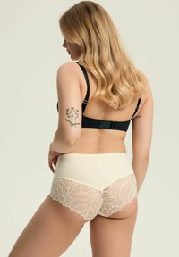 Biodra w kolorze kremowym z wysokim stanem, ozdobione przezroczystą koronką. Koronka ma wzór kwiatowy, a tył ma falbankę.