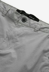 Slim fit kalhoty z jemného šedého materiálu se subtilní texturou, černým knoflíkovým zapínáním a štítkem na pasu.