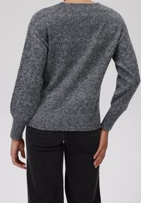 Grauer gestrickter Pullover mit strukturiertem Finish, Rundhalsausschnitt und gerippten Bündchen, kombiniert mit schwarzen Jeans. Die Rückansicht zeigt Details der Schulternaht.