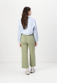 Camicia a maniche lunghe a righe azzurre, abbinata a pantaloni larghi verde oliva a vita alta con orli sfrangiati; indossando sneaker chiare.