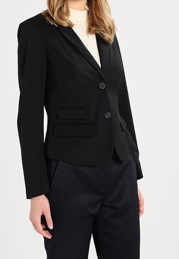 Czarna dopasowana marynarka z klapami w szpic, z przodu z guzikami i dwoma wszytymi kieszeniami. Wykonana z gładkiego materiału, zestawiona z teksturowanymi granatowymi spodniami.