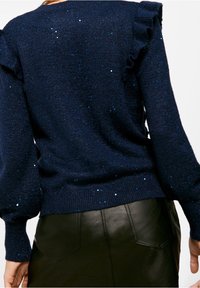 Granatowy sweter z falbankami na ramionach, z teksturowanym splotem i rozsypanymi błyszczącymi akcentami, w zestawie ze skórzaną spódnicą.
