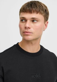 Schwarzer Sweatshirt mit Rundhalsausschnitt und texturierter Stoffoberfläche. Mit einem geprägten Logo auf der Brust, gerippten Bündchen und einem lockeren Schnitt.