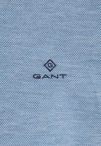 Tissu tricoté bleu clair avec logo GANT et symbole en forme de losange brodés en bleu foncé centrés.