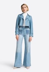 Giacca cropped in pelle blu sopra un dolcevita bianco. Jeans flare in denim azzurro chiaro con tasche a toppa a contrasto e leggero scolorimento. Scarpe beige a punta.