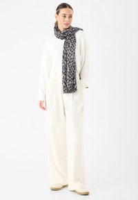 Maglione bianco, pantaloni larghi beige e una sciarpa grigia con stampa animale drappeggiata attorno al collo, completata con sneakers beige.