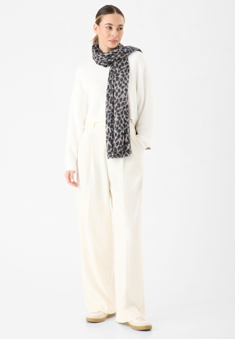 Maglione bianco, pantaloni larghi beige e una sciarpa grigia con stampa animale drappeggiata attorno al collo, completata con sneakers beige.