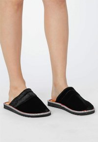 Schwarze Slipper zum Hineinschlüpfen mit einem weichen Veloursobermaterial, strukturiertem Streifen entlang des Randes und einer flexiblen Gummisohle für den Komfort.