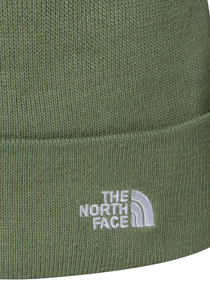 Grön stickad mössa med vikkant som har den vita broderade logotypen "The North Face".