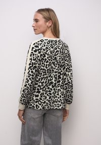 Sweter w panterkę w kolorze kremowym i czarnym, z długimi rękawami i ściągaczami u mankietów, zestawiony z jasnoszarymi dżinsami.