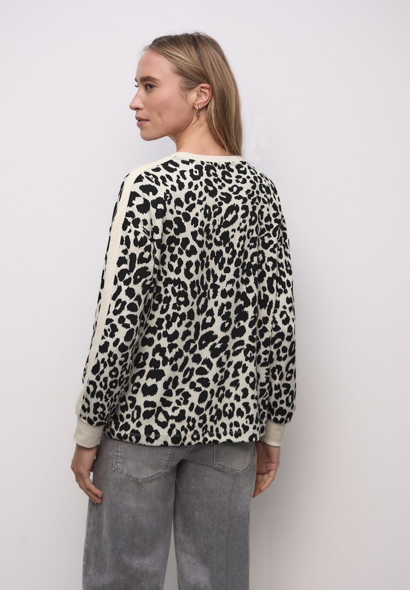 Sweter w panterkę w kolorze kremowym i czarnym, z długimi rękawami i ściągaczami u mankietów, zestawiony z jasnoszarymi dżinsami.