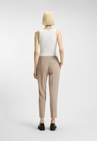 Witte mouwloze top gecombineerd met lichtbeige op maat gemaakte broeken. De broeken hebben een achterzak, een slim fit en een gestructureerd ontwerp. Zwarte plateau schoenen.