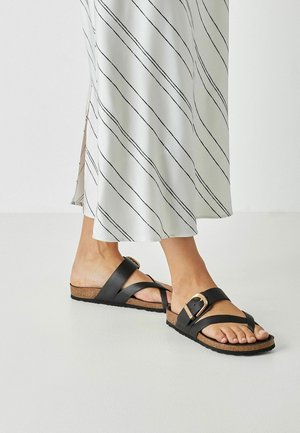 Schwarze Ledersandalen mit gekreuzten Riemen, einer dicken Korkfußsohle und einem goldfarbenen Schnallenakzent. Strukturierte Gummisohle.