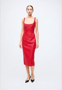 Vestido midi vermelho sem mangas, feito de pele sintética, com decote quadrado e silhueta ajustada. Usado com sapatos de salto pretos com bico fino.