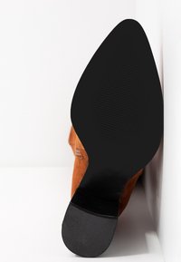Oranges Wildleder-Ankle-Boot mit einer spitzen Zehenpartie, ausgestattet mit einer strukturierten schwarzen Gummisohle und dezenten Zierstichen an der Seite.