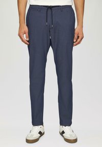 Marineblaue Hosen aus einem leichten Stoff, mit einem verstellbaren Bund, schmal zulaufenden Beinen und einem dezenten Muster. Getragen mit weißen Sneakers.