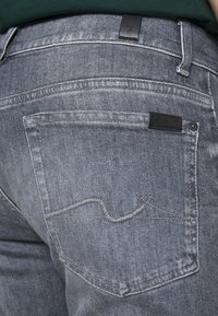 Jeans in denim grigio con una finitura texture. Presentano una patch in pelle nera e cuciture a contrasto sulla tasca posteriore. Design classico a cinque tasche.