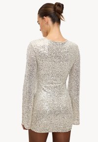 Robe en sequins argentés à manches longues et silhouette ajustée. Elle présente un col rond et un ourlet court. Texture lisse sur toute la surface.