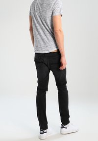 Vaqueros slim fit negros con cinco bolsillos, combinados con una camiseta de manga corta gris jaspeada y zapatillas blancas con detalles en azul marino.