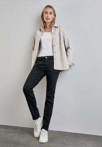 Ljusbeige skjorta med knappar, vit linne t-shirt, svarta slim-fit jeans och vita sneakers. Slät textur, avslappnad design.