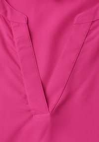 Gros plan sur un tissu magenta montrant un col en V avec un large revers cousu et une texture lisse.