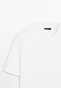 T-shirt blanc uni à manches courtes et col rond, avec une étiquette noire à l’intérieur du col, présenté sur fond blanc. Aucun logo ou motif visible.