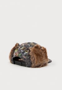 Čiapka s camo potlačou, mäkkými hnedými umelými kožušinovými ušnými chlopňami a plastovým zapínaním na zacvaknutie. Má okrúhly tvar a vzorovanú látku.