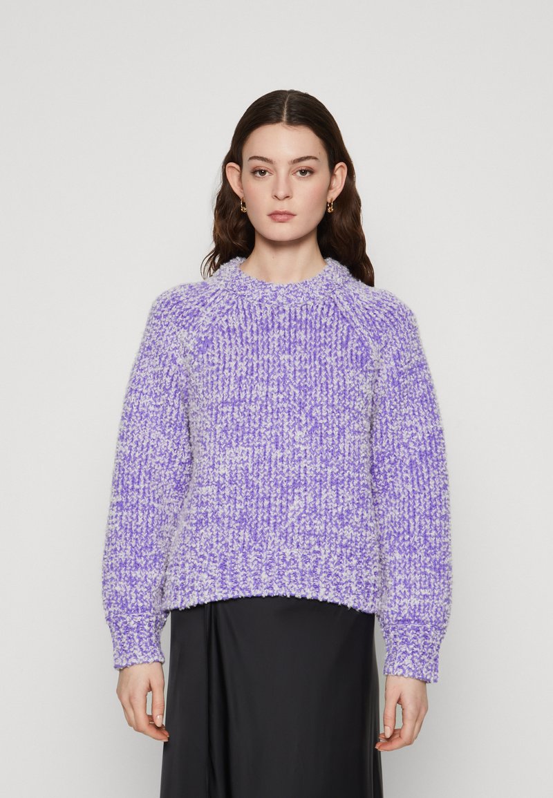Maglione viola lavorato a maglia con una superficie texturizzata e soffice. Presenta un collo rotondo, maniche lunghe e una vestibilità rilassata. Abbinato a una gonna nera.